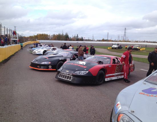 Race cars lined up on a track with drivers and crew members standing nearby.