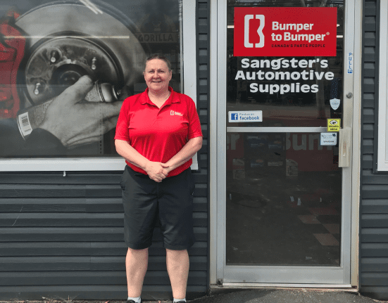Person in a red shirt standing in front of Sangsters Automotive Supplies, with a large brake disc image on the window.