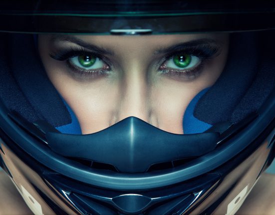 Close-up of a person wearing a full-face motorcycle helmet, with striking green eyes visible through the visor.