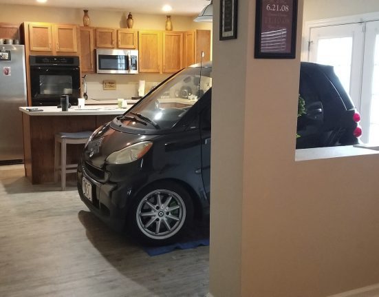 A small car is parked inside a kitchen area with wooden cabinets, a refrigerator, and an island counter.