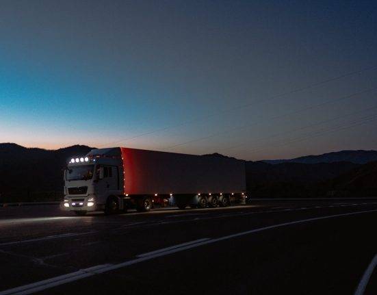 A semi-truck on a long highway under dark skies