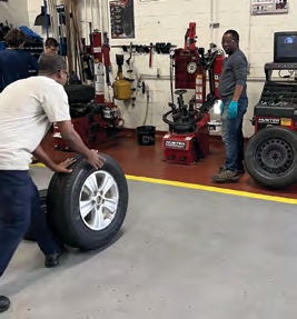One individual guiding a tire towards the machine while another person waits to help them